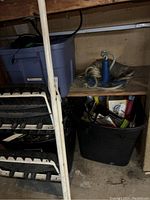 Photo of a white metal step ladder, blue metal anchor with rope, and storage bins in a garage shelving unit.