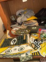 Photo showing various Green Bay Packers memorabilia on a surface, includes several fabric items, plaques, cups, newspapers, and books.