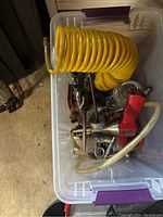 Photo of a clear plastic tackle box containing coiled bright yellow air hose, red electric tool, metal fittings and hand tools