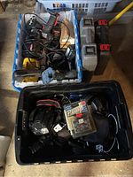 View of two boxes: one with Skill power tools with cords and chargers, yellow power tool, other with toolboxes; black plastic bin with camera and accessories including Brother P-touch label cassette and cables.
