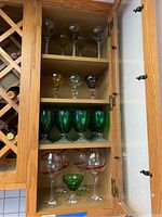 Full cabinet view showing four shelves of various vintage glassware including red rim wine glasses, green goblets, multi-colored cordial glasses, and twisted stem glasses.