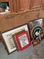 Photo showing a collection of framed wall art and decorative pieces leaning against a wood cabinet.