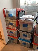 Seven plastic storage bins stacked containing various women's clothing items organized and labeled by size and type