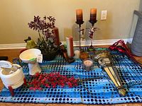 Various candles, flower stems, decorative pears, metal wall art and candle holders arranged on blue polka dot cloth