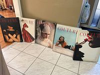 Five stretched canvas prints arranged in a row on a tiled floor against a wall, showing various women in couture fashion