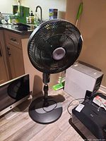 Front view of black Weather Works floor fan with pedestal base, showing its size and design in room environment