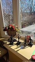 Photo showing the three abstract black sculptures and the faux floral centerpiece on a windowsill with natural light.