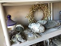 Elephant boot scraper, reed wreath, ceramic bird feeder with purple top, multiple resin wall plaques arranged on shelf