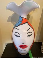 Front view of white glass vase with ruffled top and stylized red-haired woman's face design