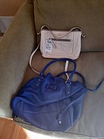 Two Kate Spade purses on a green couch - one blue tote and one beige crossbody bag visible