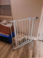 White metal pet gate against a wall with pressure mount ends and small built-in swinging pet door near the floor.