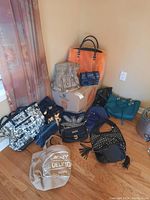 Overview photo showing collection of various purses and bags grouped around a cardboard box on the floor including large printed tote and furry orange handbag.