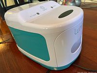 Left side and top angled view of white and teal sanitizer device with control lights and 'Lumin' branding.