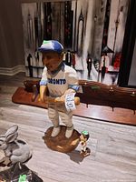 Both the 25-inch Toronto baseball player statuette and the 6-inch basketball bobblehead shown on wooden floor with furniture backdrop.