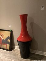 Front view of the tall ceramic vase showing its two-toned red and black color and glossy finish. Vase is tall and slender with a wide base.