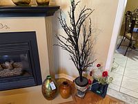 Wide view showing all items grouped by fireplace including two vases, faux tree, flower wall art, and metal tray