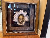 Front view of shadow box wall art with mask and curled musical note paper sculpture, framed in a wooden beaded frame.