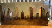 Full frontal view of the wood and canvas wall art showing the stylized cityscape design and artist signature.