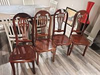 Photo showing four wooden dining chairs with slight scratches and polished finish.