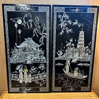 Full view of two black lacquer panels illustrating Asian scenes with figures, architecture, and nature in silver inlay.
