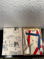 Top view of a box containing the scarves including a glimpse of a red, white, and blue striped scarf inside