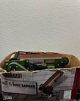 Photo showing the Central Machinery belt and disc sander partially inside the original box with a label showing the model and belt size.