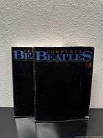 Front view of two Complete Beatles Song Books, showing the black covers with the title in blue and white.