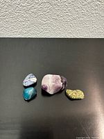 Four small polished gemstones arranged on a black surface against a textured wall backdrop, showing different angles and grouping.