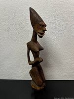 Full side view of the carved wooden African sculpture showing the elongated head and detailed facial features.