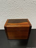 Front view of a small rectangular teak wooden box showing the natural wood grain and smooth finish.