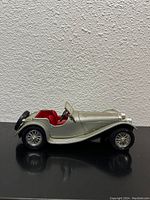 Side view of silver 1937 Jaguar SS 100 model car showing red interior and black spare tire.