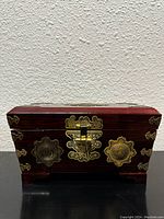 Front view of vintage wooden jewelry box showing metal latch and decorative accents