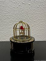 Side view of the vintage caged songbird music box showing the cage, red bird, and decorative base.