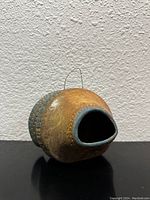 Side view of rounded vintage terra cotta pot with carved details and hanging wire, showing open front mouth and blue accent glaze.