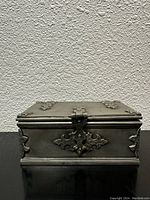 Front view of the rectangular vintage metal box showing ornate latch and hinges.