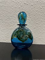 Front view of vintage blue glass bottle with hand-painted details and stopper on top.