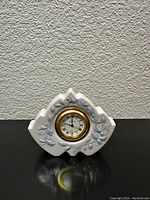 Front view of the vintage LLADRO porcelain tabletop clock with floral embossed design surrounding the clock face.