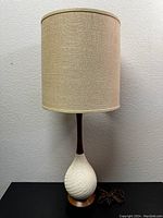 Full view of the vintage Mid Century Modern table lamp showing the beige fabric drum lampshade, dark wood neck, textured cream ceramic base, and wooden base platform.