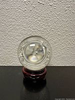Front view of the clear crystal ball on a carved wooden stand against a textured wall.
