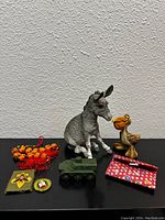 Photo showing all items in the lot including donkey and pelican figurines, toy military vehicle, bead string, patches, and pouch.