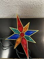 Full view of the star-shaped Bethlehem light showing red, blue, orange, and teal colored plastic segments with gold trim and electrical cord.