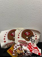 Photo showing two vintage Official San Francisco 49ers placemats with a gold helmet logo and multiple bandanas in front, plus a red KGO Newstalk AM 810 football-themed bandana.