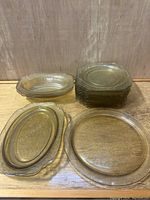 Top view of stacked square plates, three oval serving bowls, and one large round plate showing Madrid pattern and yellow Depression glass characteristics