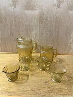 Full view of the six piece vintage yellow Depression glass Madrid pattern lot, including two pitchers, two small handled creamers, and two handled sugar bowls.