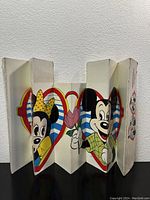 Folded vintage Disney car windshield sun shade featuring front illustration of Mickey and Minnie Mouse inside hearts with a striped background.