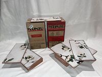 Two boxes of Mainzu ceramic tiles with floral patterns, including some loose tiles stacked in front showing the design.