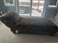 Full side view of antique chaise lounge upholstered in dark floral fabric with carved gold-tone wood trim and legs.