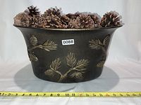 Front view of the pinecone container filled with pinecones and a measuring tape showing the width at approximately 14 inches.