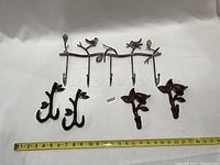 Full view of all five bird-themed metal wall hangers arranged on white background with measuring tape showing length.