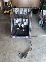 Front view of the Allen T2 bicycle trailer showing the two child seats with harnesses and the tow arm for bicycle attachment, stored in a garage.